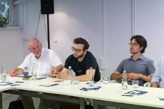Trzech mężczyzn siedzących przy stole, prowadzących dyskusję w sali konferencyjnej.