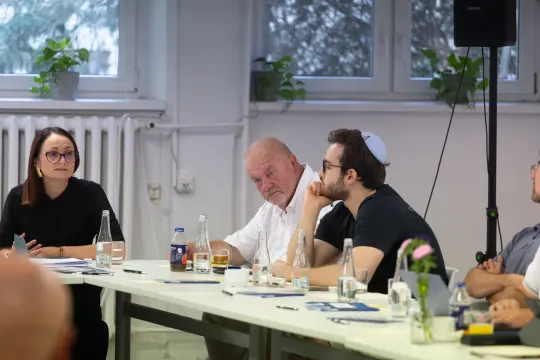 Spotkanie grupy ludzi przy stole, dyskusja, notatki, napoje.
