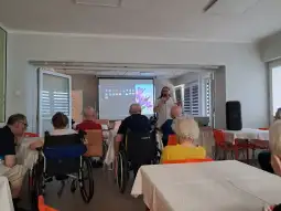 Prezentacja dla seniorów w sali z krzesłami i stołami.
