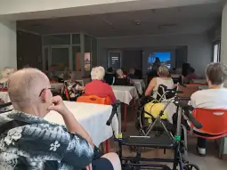 Spotkanie w sali dla seniorów z prezentacją na ekranie.
