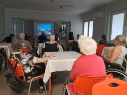 Spotkanie grupy seniorów w sali wykładowej z prezentacją na ekranie.