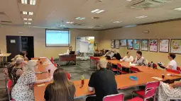 Spotkanie grupy ludzi w sali konferencyjnej z prezentacją na ekranie.