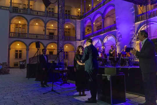 Ceremonia wręczenia nagrody w oświetlonym dziedzińcu z muzykami w tle.