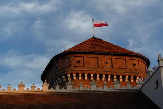 Czerwony dach z białą flagą Polski na tle nieba.