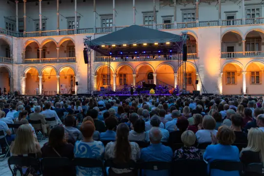 Koncert na świeżym powietrzu z widownią w eleganckim otoczeniu architektonicznym.