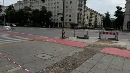 Zniszczona nawierzchnia chodnika przy skrzyżowaniu, oznaczenia robót drogowych.
