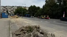 Roboty drogowe, usunięte fragmenty nawierzchni, pojazdy na ulicy, budynki w tle.