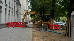 Prace budowlane na ulicy z koparką i barierkami ochronnymi.