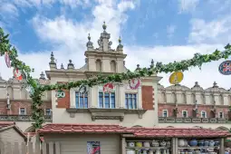 Budynek z ozdobnym dachem i dekoracjami, otoczony zielonymi pnączami i kolorowymi girlandami.