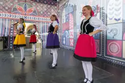 Cztery tancerki w tradycyjnych strojach ludowych tańczą na scenie.