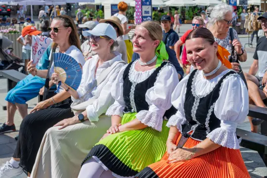 Grupa kobiet w tradycyjnych strojach ludowych siedzących na ławce.