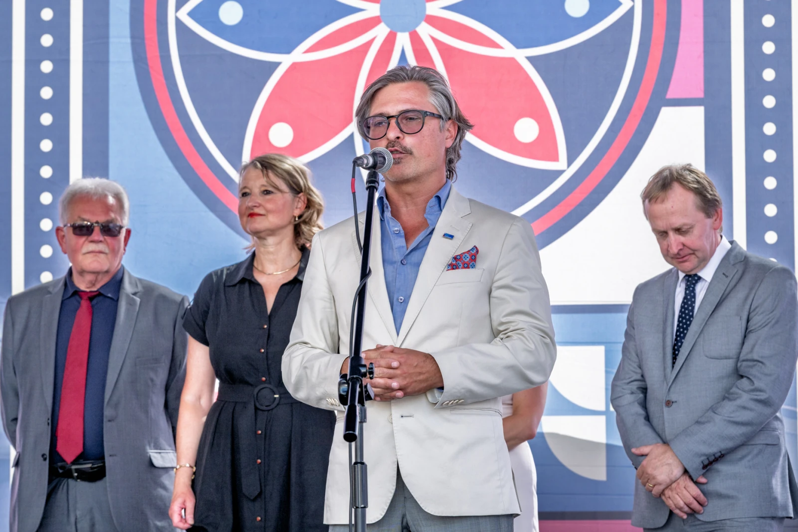 Mężczyzna w jasnym garniturze przemawia do mikrofonu, obok stoją trzy osoby.  Autor: Piotr Wojnarowski