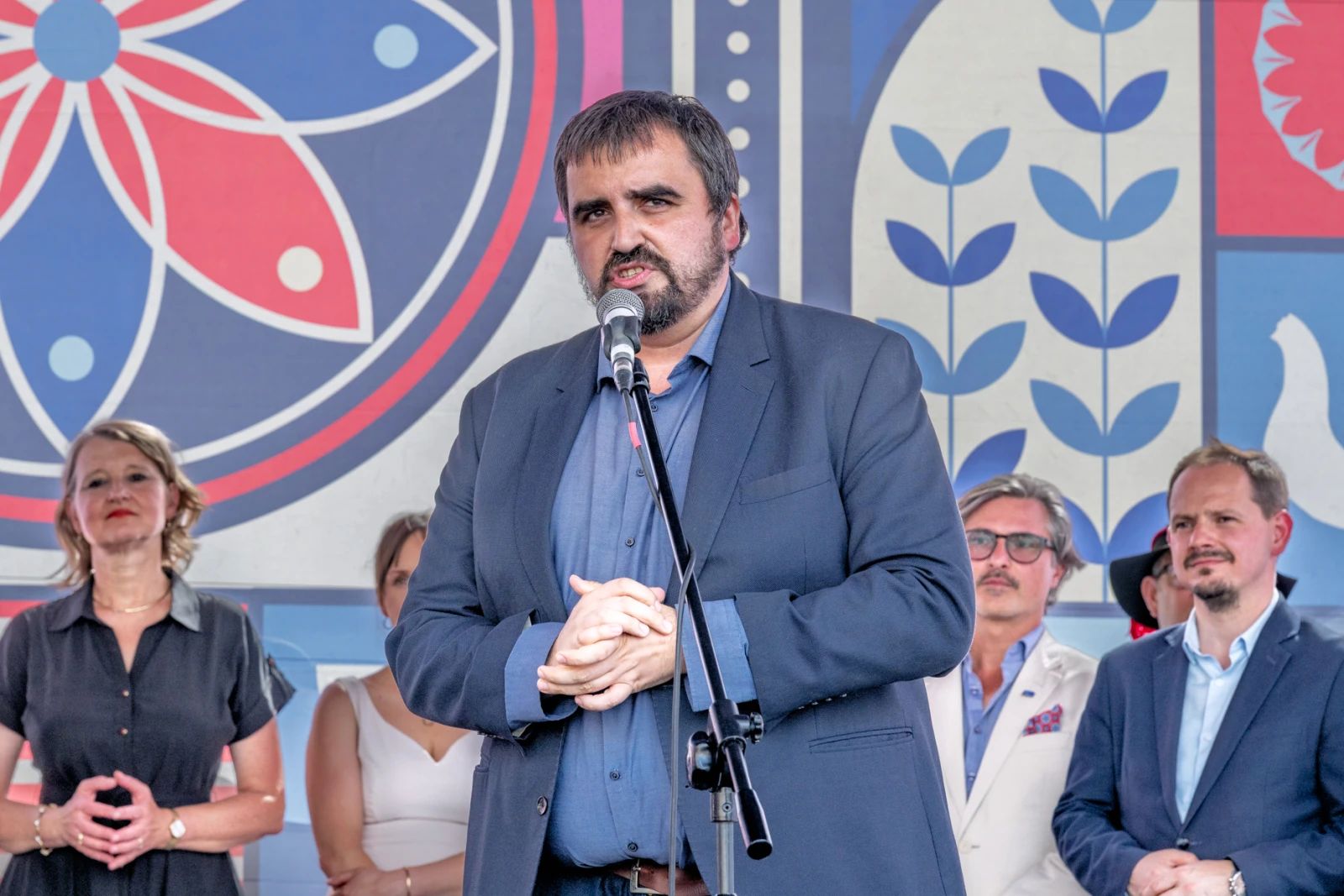 Mężczyzna w garniturze przemawia do mikrofonu, w tle grupa osób.  Autor: Piotr Wojnarowski