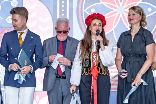 Cztery osoby na scenie, jedna w tradycyjnym stroju, przemawia do publiczności.