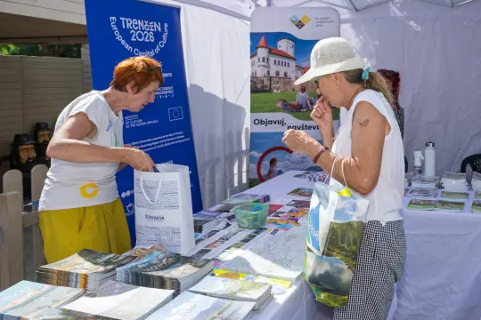 Kobiety przeglądają materiały promocyjne na stoisku informacyjnym.