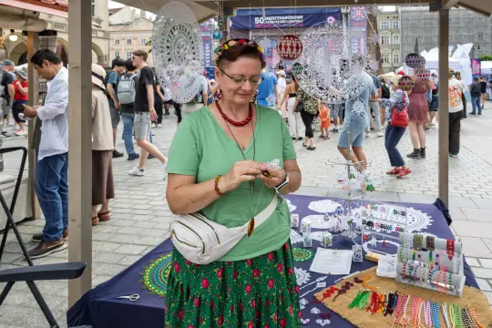 Kobieta w tradycyjnym stroju ludowym sprzedaje rękodzieło na festiwalu.