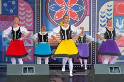 Grupa tancerek w kolorowych spódnicach wykonująca tradycyjny taniec ludowy.