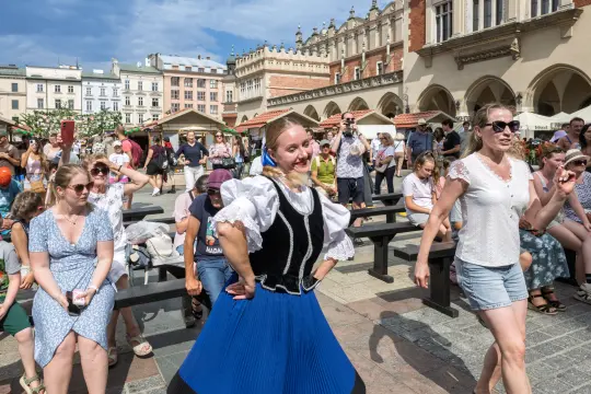 Kobieta w tradycyjnym stroju tańczy na rynku, wokół niej tłum ludzi.