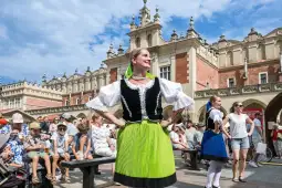 Kobieta w tradycyjnym stroju ludowym tańcząca na tle historycznej architektury.