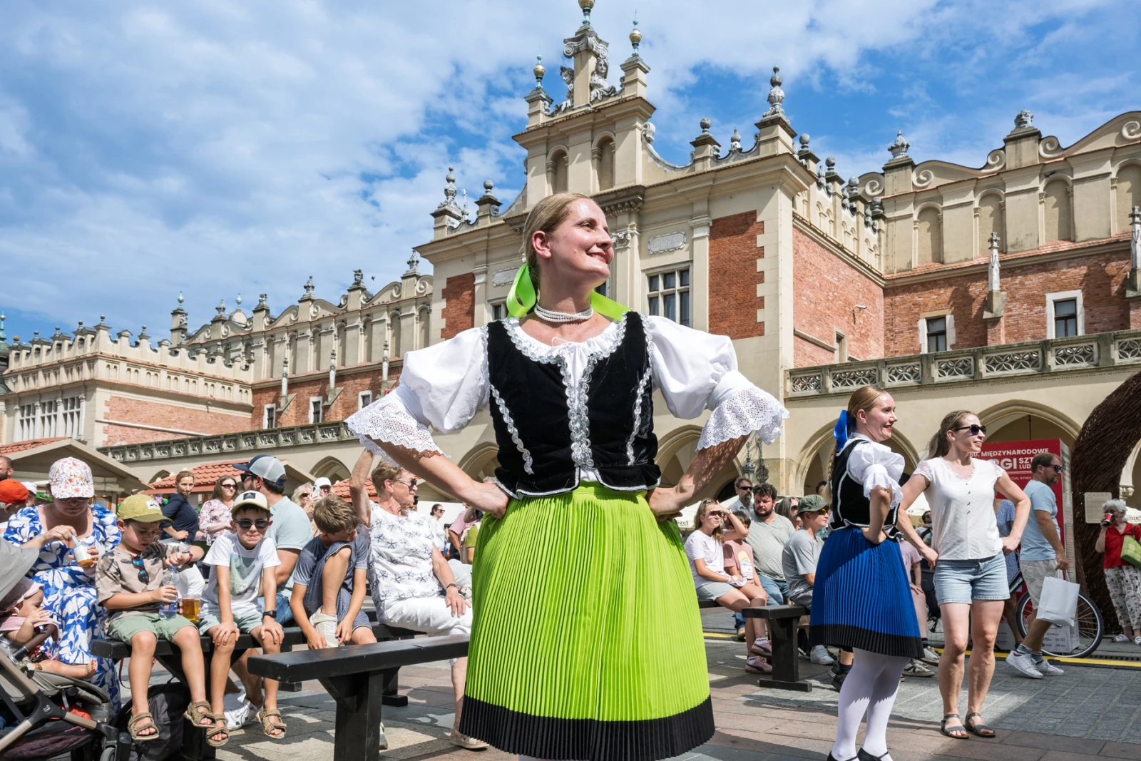 Kobieta w tradycyjnym stroju ludowym tańcząca na tle historycznej architektury.  Autor: Piotr Wojnarowski