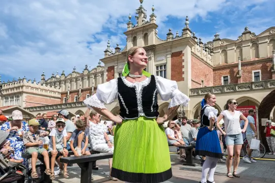 Kobieta w tradycyjnym stroju ludowym tańcząca na tle historycznej architektury.