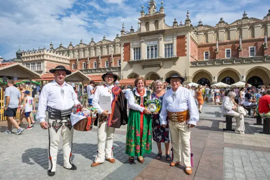 Grupa osób w tradycyjnych strojach ludowych na tle zabytkowej architektury.