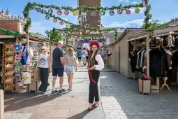 Kobieta w tradycyjnym stroju ludowym na festiwalu, otoczona straganami i dekoracjami.