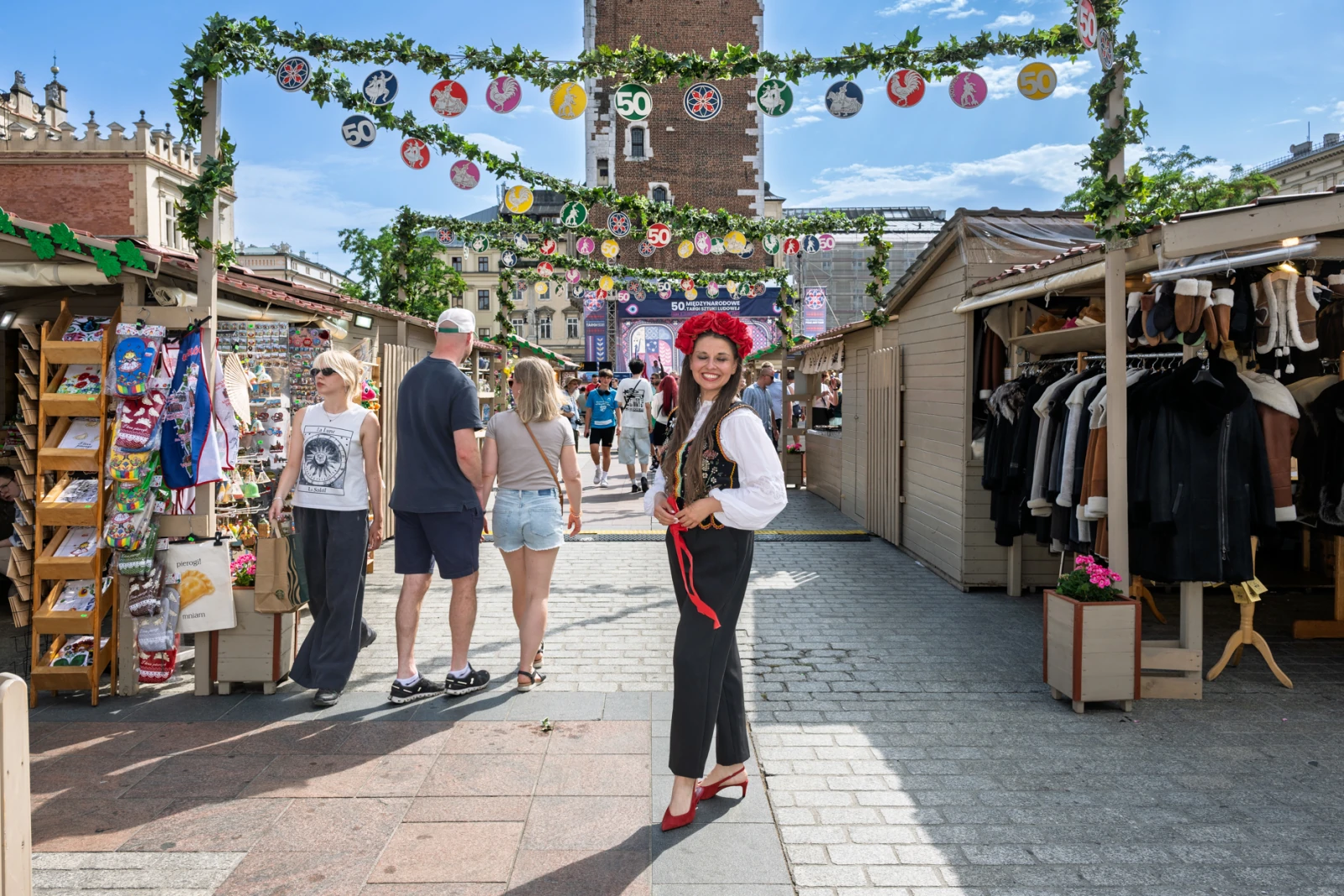 Kobieta w tradycyjnym stroju ludowym na festiwalu, otoczona straganami i dekoracjami.  Autor: Piotr Wojnarowski