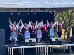 Dzieci w tradycyjnych strojach ludowych tańczą na scenie podczas występu.