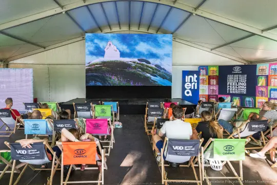 Widownia oglądająca film w namiocie festiwalowym, z ekranem i kolorowymi krzesłami.