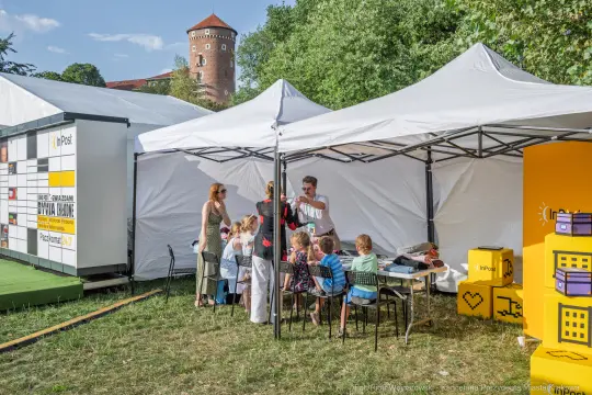 Dzieci bawią się w namiocie na festiwalu, obok rodzice i stoiska z atrakcjami.