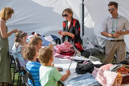 Grupa dzieci i dorosłych przy stole, sortujących ubrania w plenerze.