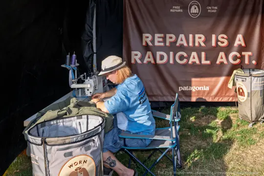 Kobieta naprawiająca odzież przy maszynie do szycia, z hasłem o naprawach w tle.