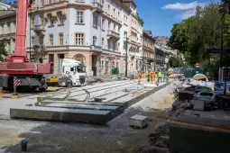 Prace budowlane na ulicy, w tle ciężki sprzęt i robotnicy w kamizelkach odblaskowych.