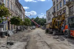 Ulica w trakcie remontu z maszynami budowlanymi i drzewami po obu stronach.