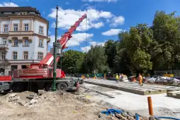 Budowa drogi z dźwigiem i pracownikami w otoczeniu zieleni i budynków.