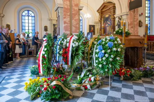 Uroczystość pogrzebowa z wieńcami i kwiatami w kościele.