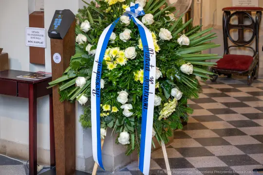 Wieniec z białymi różami i żółtymi kwiatami, z niebieskimi wstęgami.