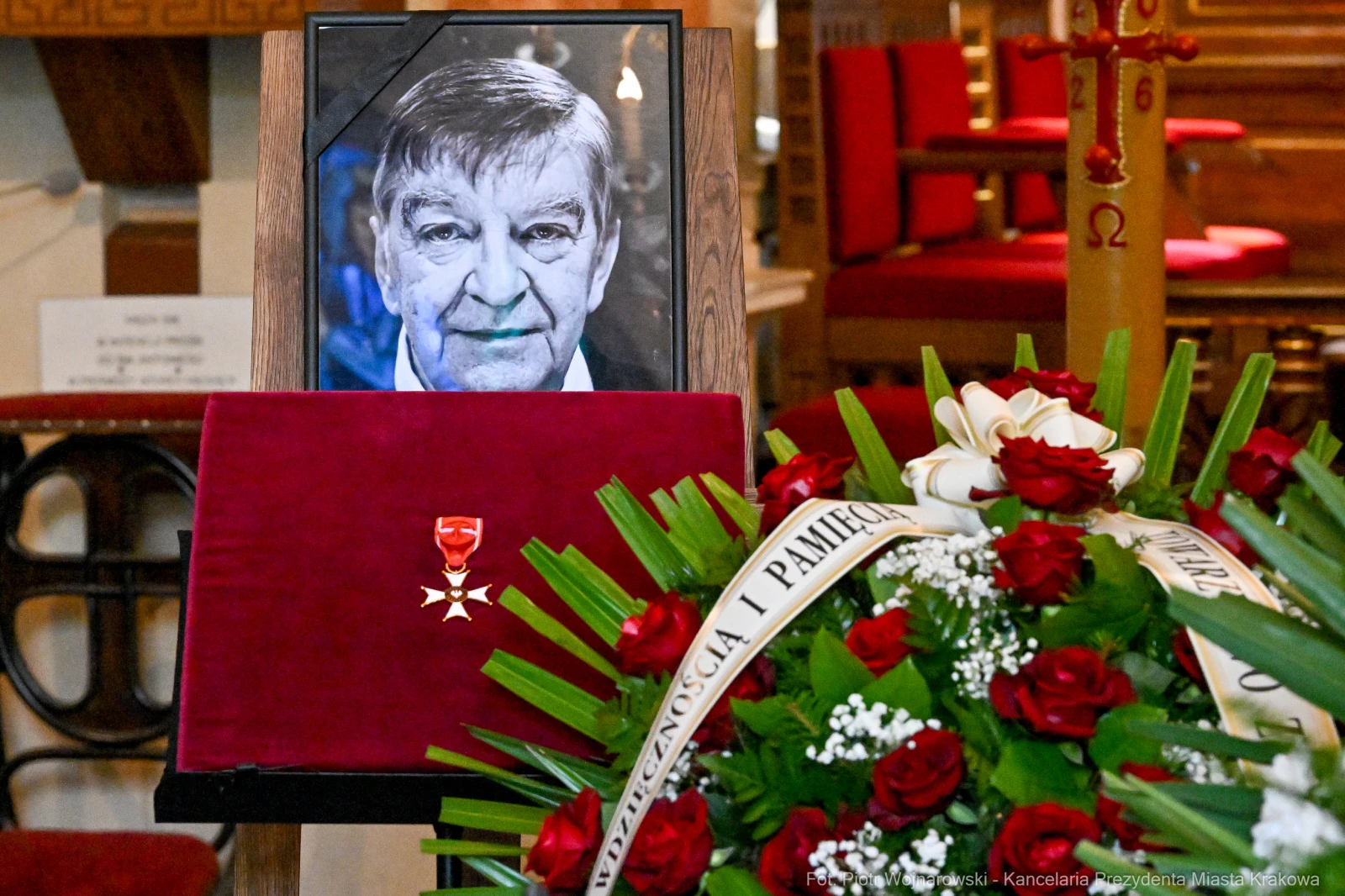 Portret mężczyzny obok czerwonego pudełka z odznaczeniem i bukietem czerwonych róż.  Autor: Piotr Wojnarowski