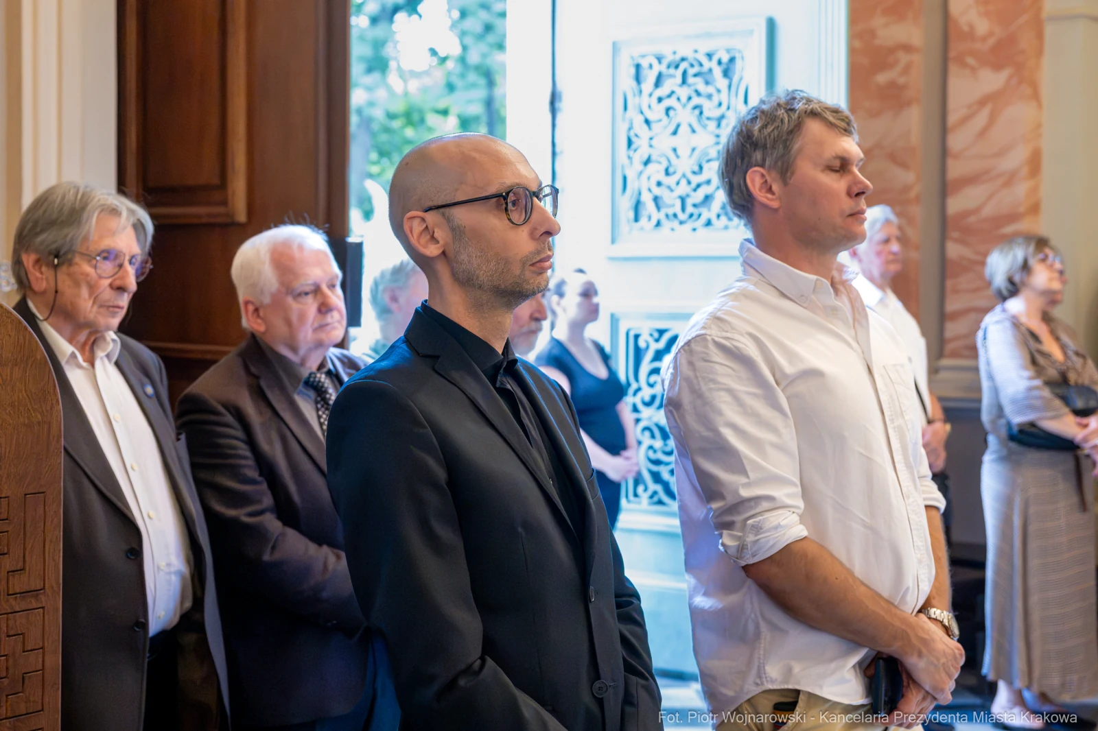 Grupa osób stojących w eleganckim wnętrzu, niektórzy w formalnych strojach.  Autor: Piotr Wojnarowski