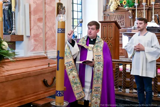 Kapłan w ornacie błogosławi świecę obok trumny w kościele.