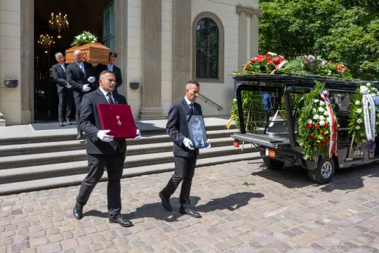 Pogrzeb z trumną, mężczyźni w garniturach niosący zdjęcie zmarłego.