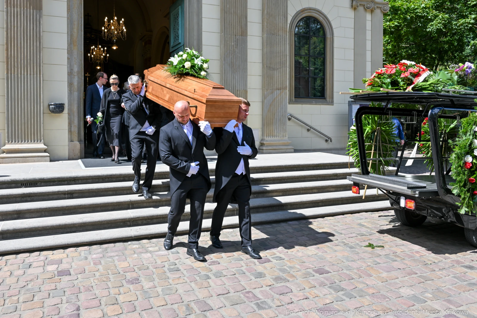 Pogrzeb z trumną niesioną przez mężczyzn w garniturach, otoczony przez żałobników.  Autor: Piotr Wojnarowski