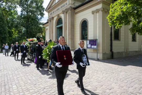 Pogrzeb z trumną i żałobnikami niosącymi zdjęcie zmarłego.