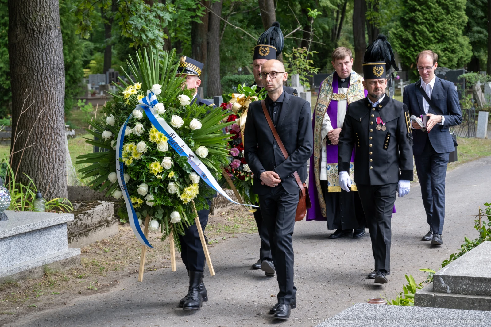 Pogrzeb z uczestnikami niosącymi wieniec i duchownym w otoczeniu cmentarza.  Autor: Piotr Wojnarowski