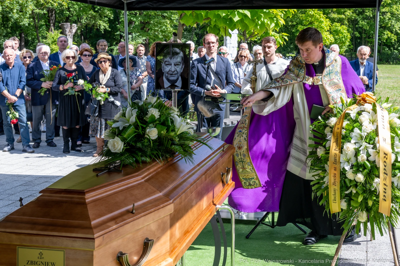 Ceremonia pogrzebowa z trumną i osobami w żałobie, w tle portret zmarłego.  Autor: Piotr Wojnarowski
