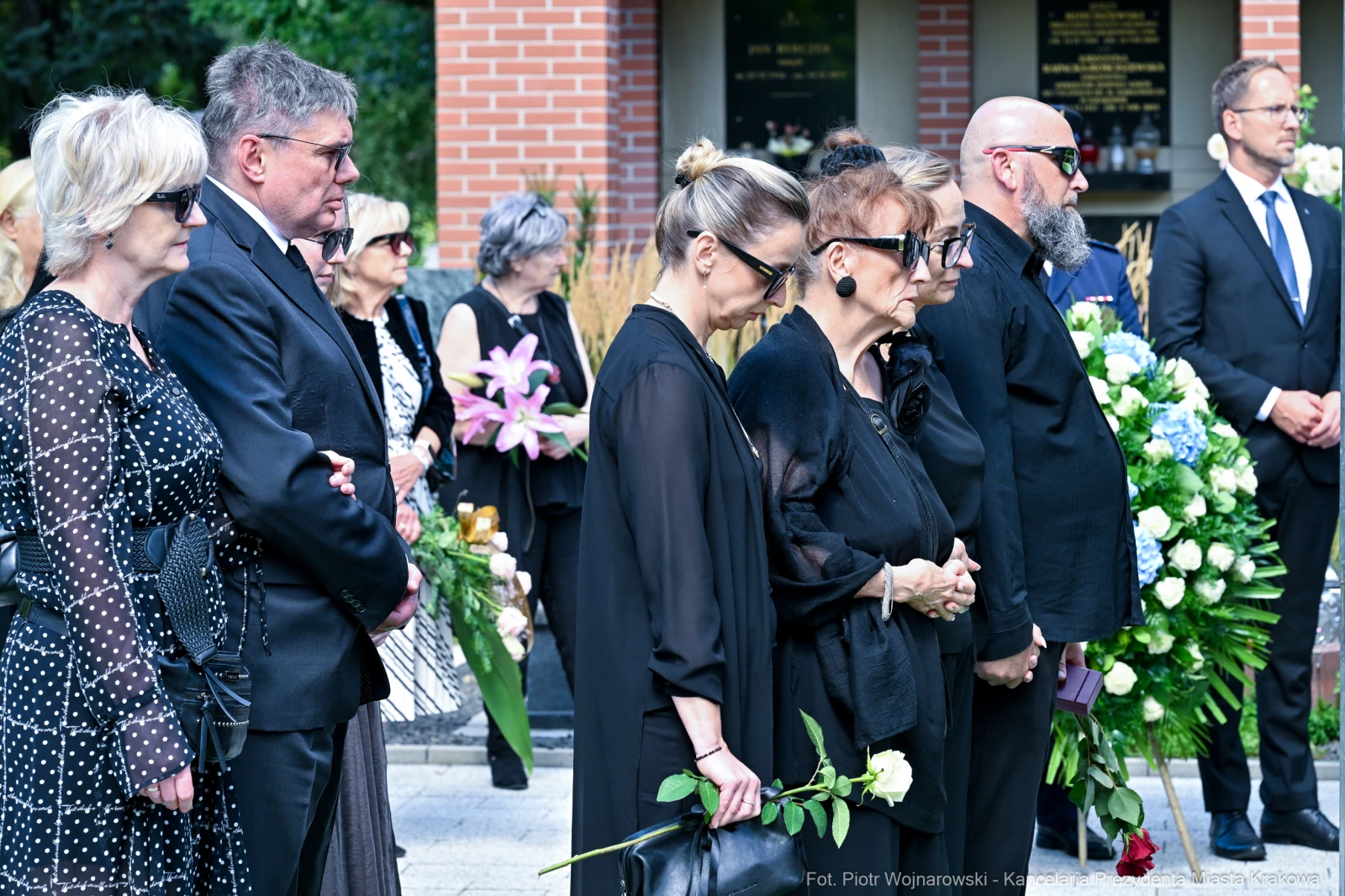 Grupa osób w czarnych strojach podczas ceremonii pogrzebowej, trzymających kwiaty.  Autor: Piotr Wojnarowski