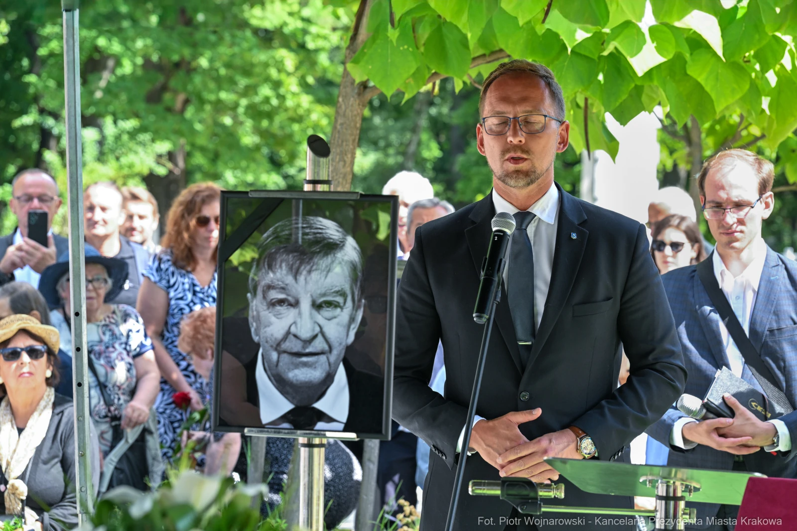 Ceremonia upamiętniająca zmarłego, mężczyzna przemawia przed portretem. W tle zgromadzeni goście.  Autor: Piotr Wojnarowski