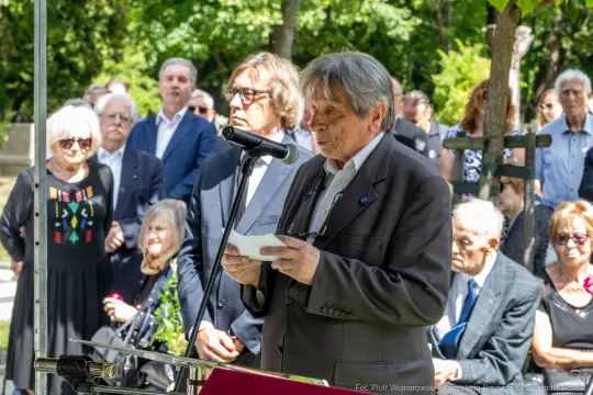 Mężczyzna przemawia do zgromadzonego tłumu podczas uroczystości na świeżym powietrzu.
