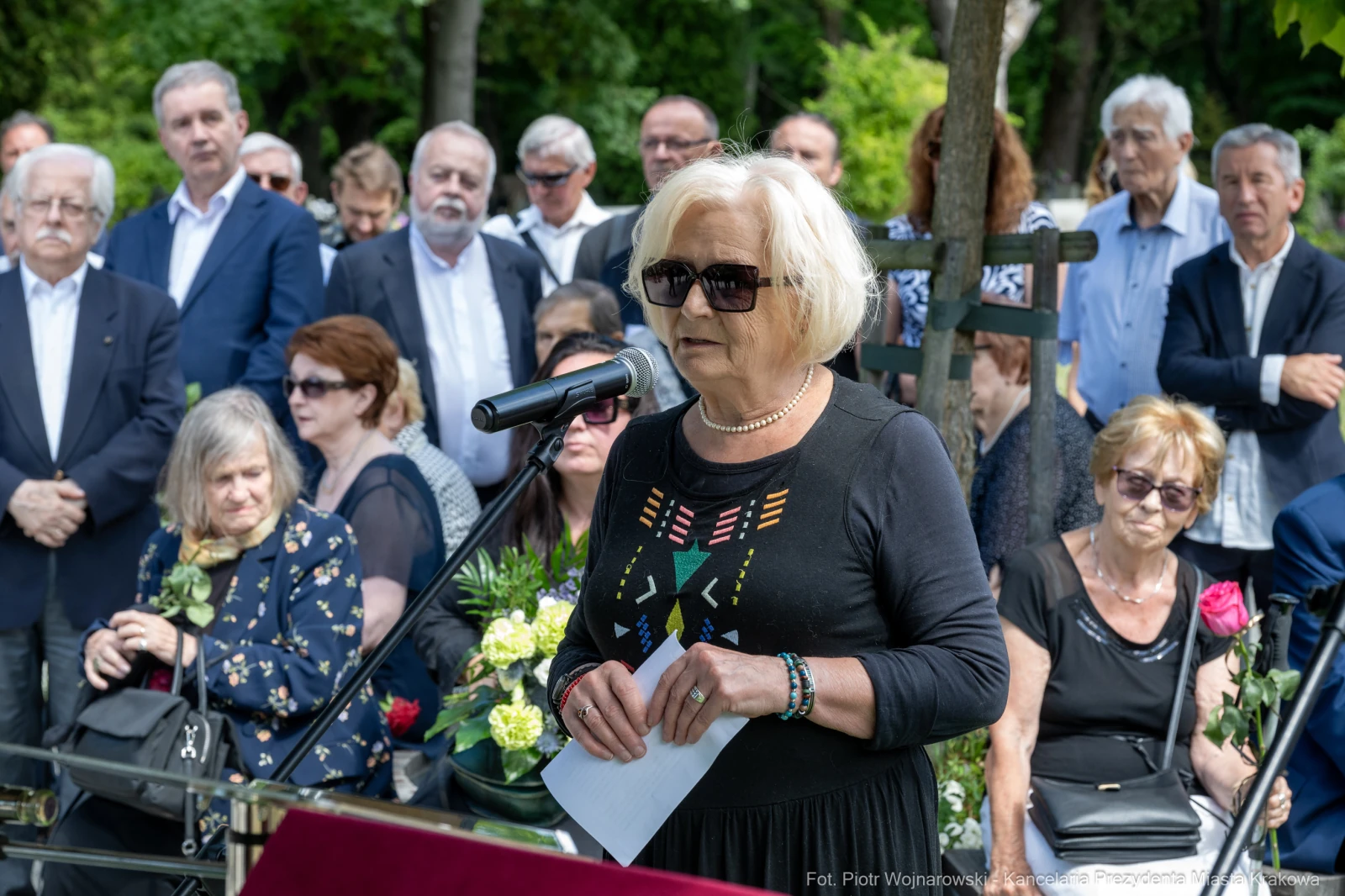 Kobieta w okularach przeciwsłonecznych przemawia do zgromadzonych na ceremonii pogrzebowej.  Autor: Piotr Wojnarowski